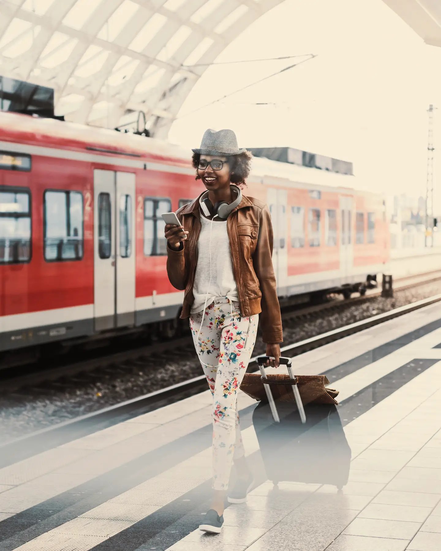 Eine Frau läuft mit einem Koffer am Bahnsteig entlang, im Hintergrund ein roter Zug der deutschen Bahn.
