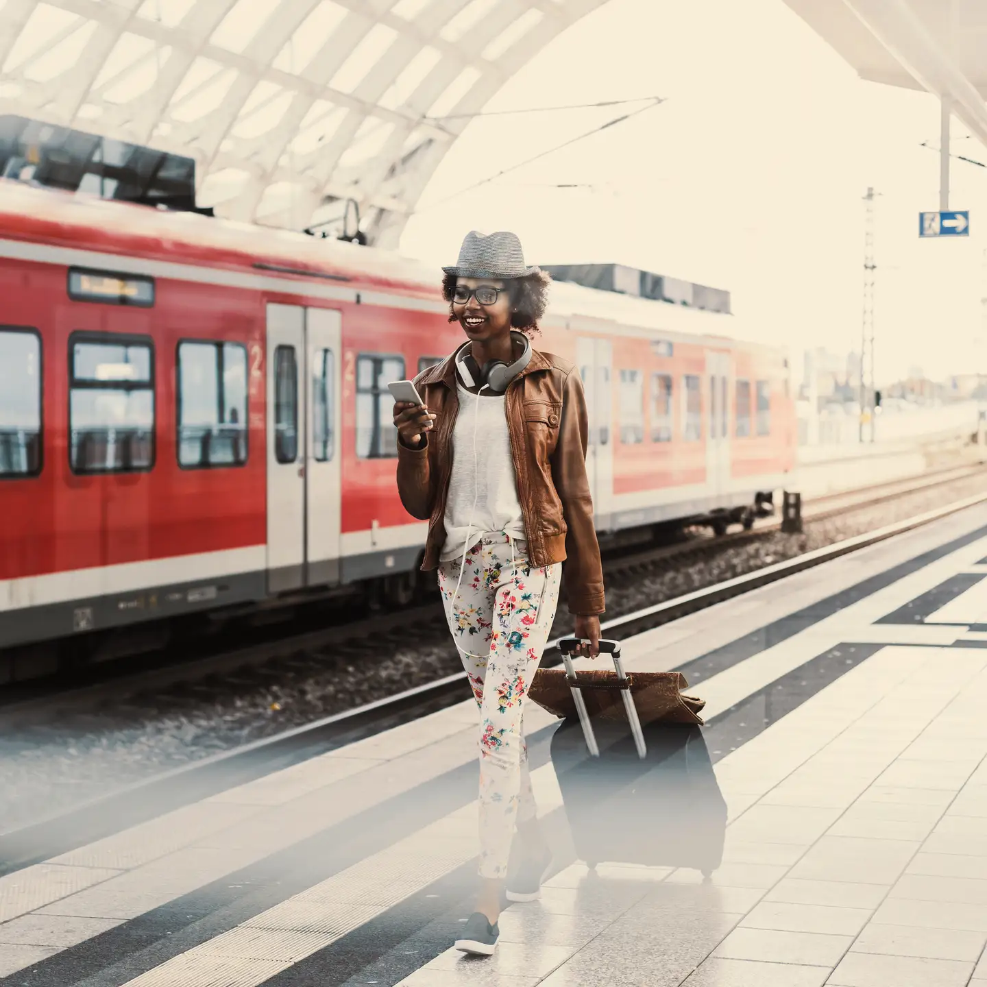 Eine Frau läuft mit einem Koffer am Bahnsteig entlang, im Hintergrund ein roter Zug der deutschen Bahn.