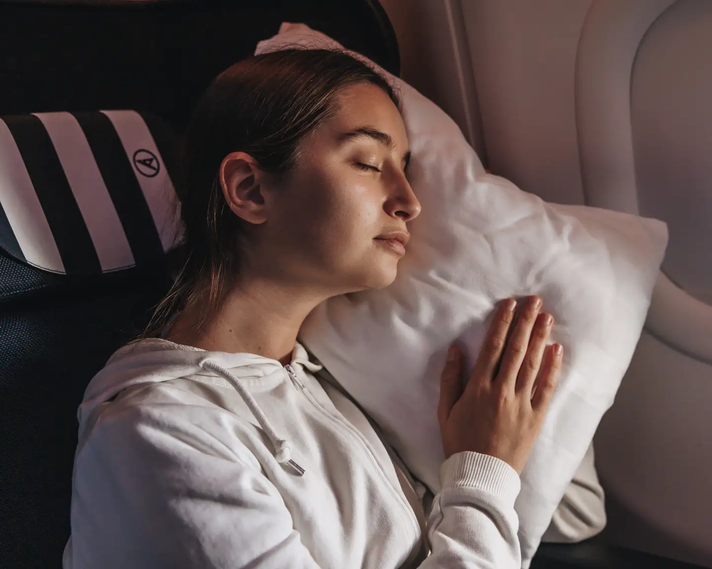 Mujer dormida en un avión, con la cabeza apoyada en una almohada contra la ventanilla.