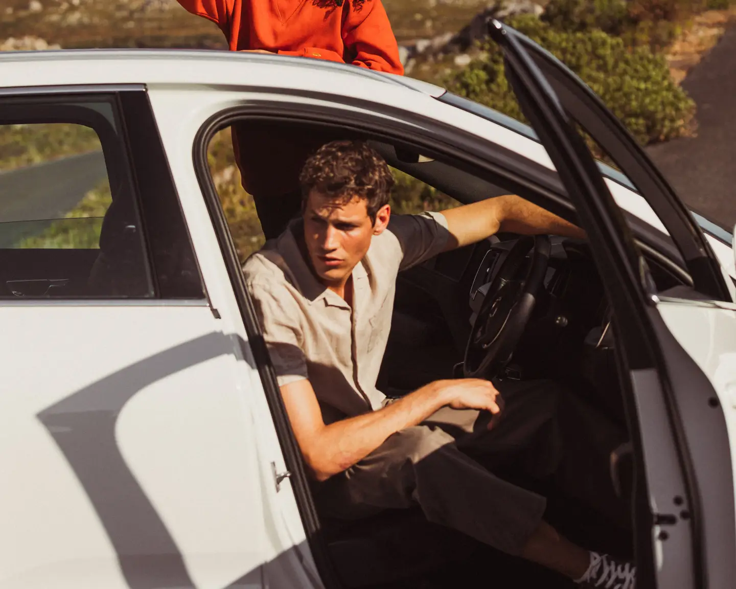 A woman standing through a car's sunroof, smiling and pointing, while a man sits in the driver's seat, both enjoying a scenic drive through a mountainous landscape.