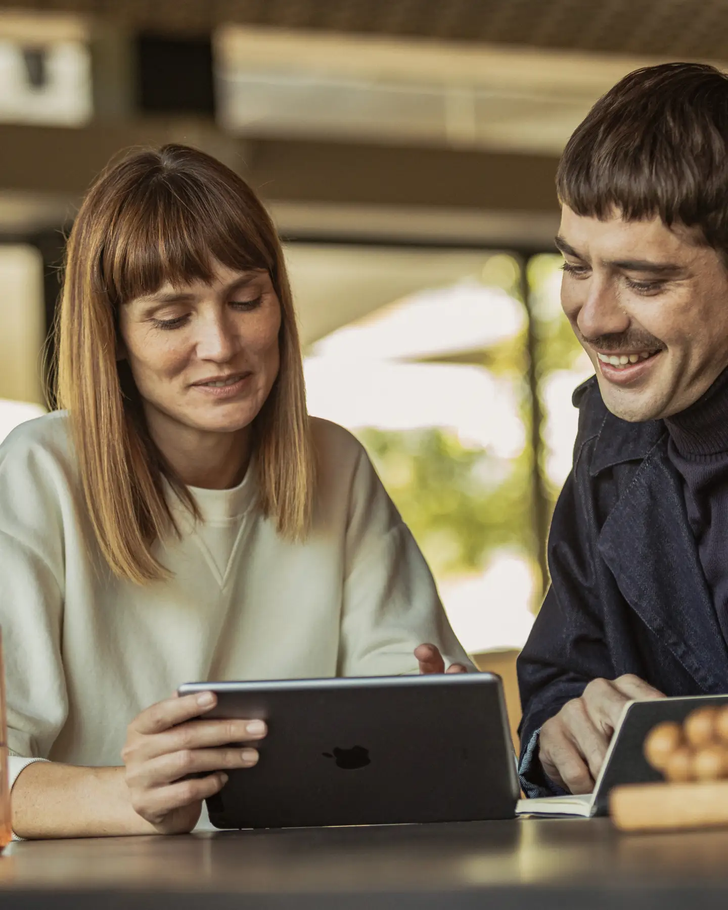 Un jeune homme et une jeune femme sont assis à une table et regardent leur tablette.