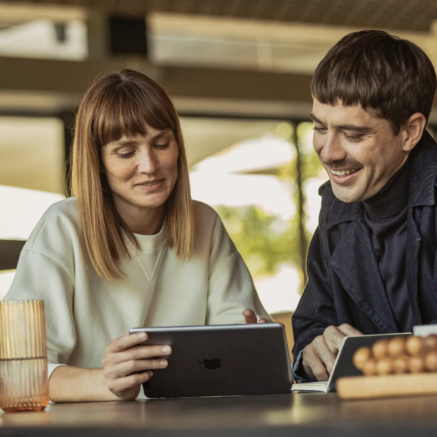 Un jeune homme et une jeune femme sont assis à une table et regardent leur tablette.