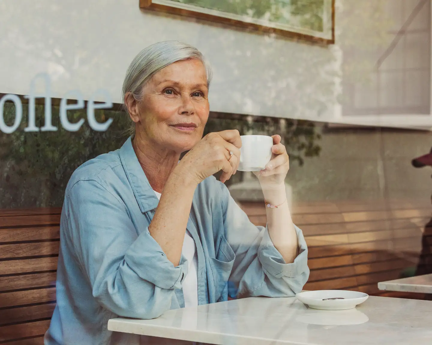 Señora mayor sentada en una cafetería sujetando una taza de café.