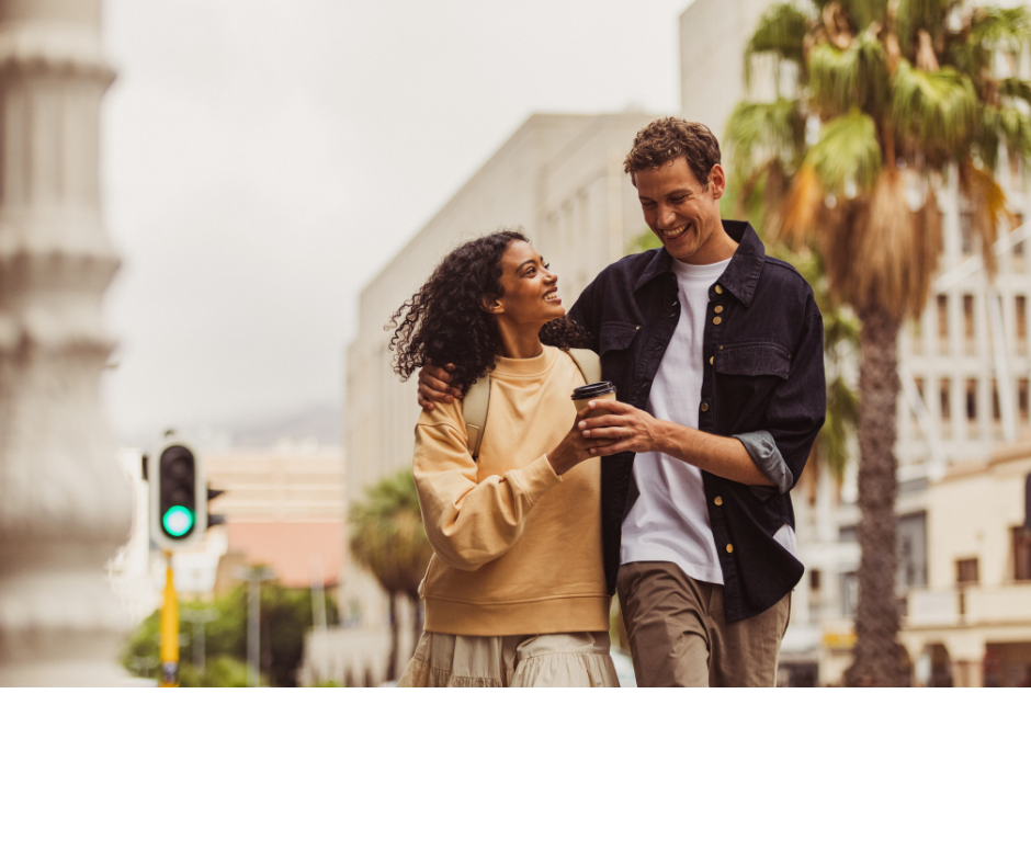 Two travelers walk together with a drink through a palm-lined city.