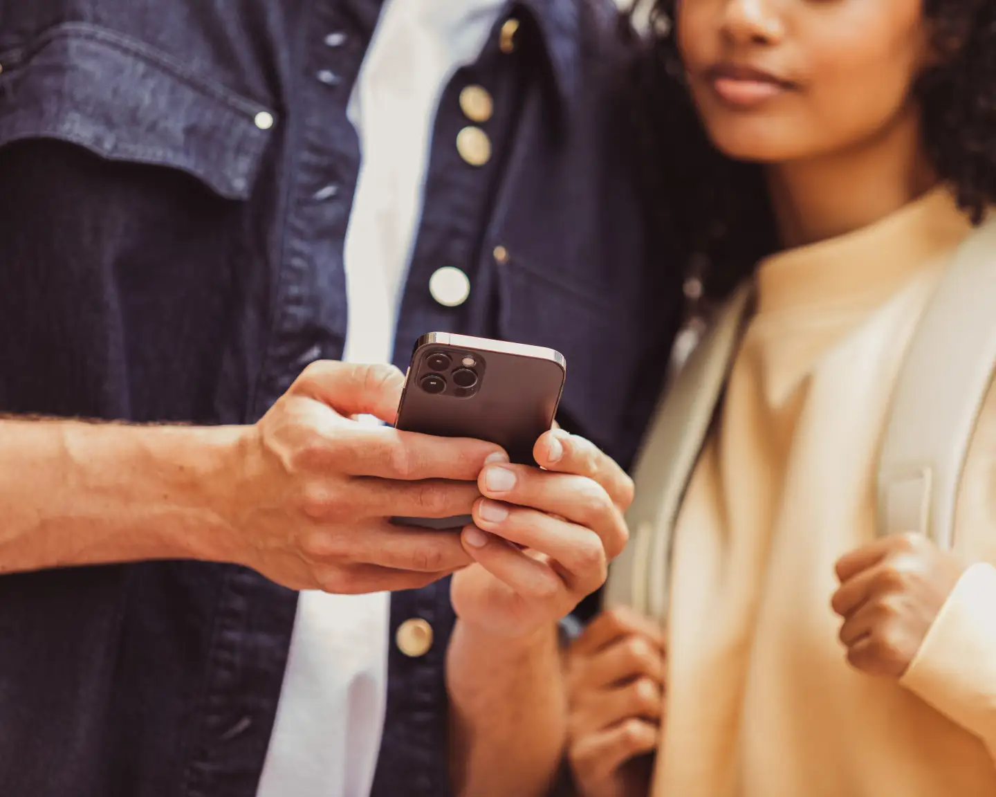 Een detail van een stel, waarbij alleen hun bovenlichamen zichtbaar zijn en hun handen samen een smartphone vasthouden.
