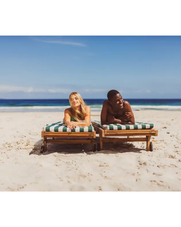 Zwei Reisende entspannen auf Sonnenliegen an einem weißen Sandstrand mit Blick auf das Meer.