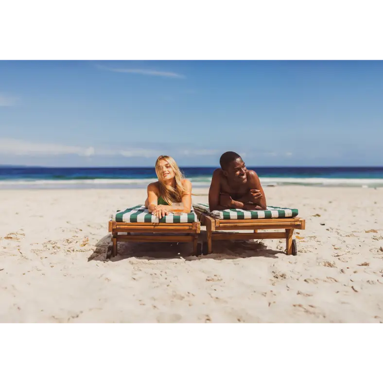 Zwei Reisende entspannen auf Sonnenliegen an einem weißen Sandstrand mit Blick auf das Meer.