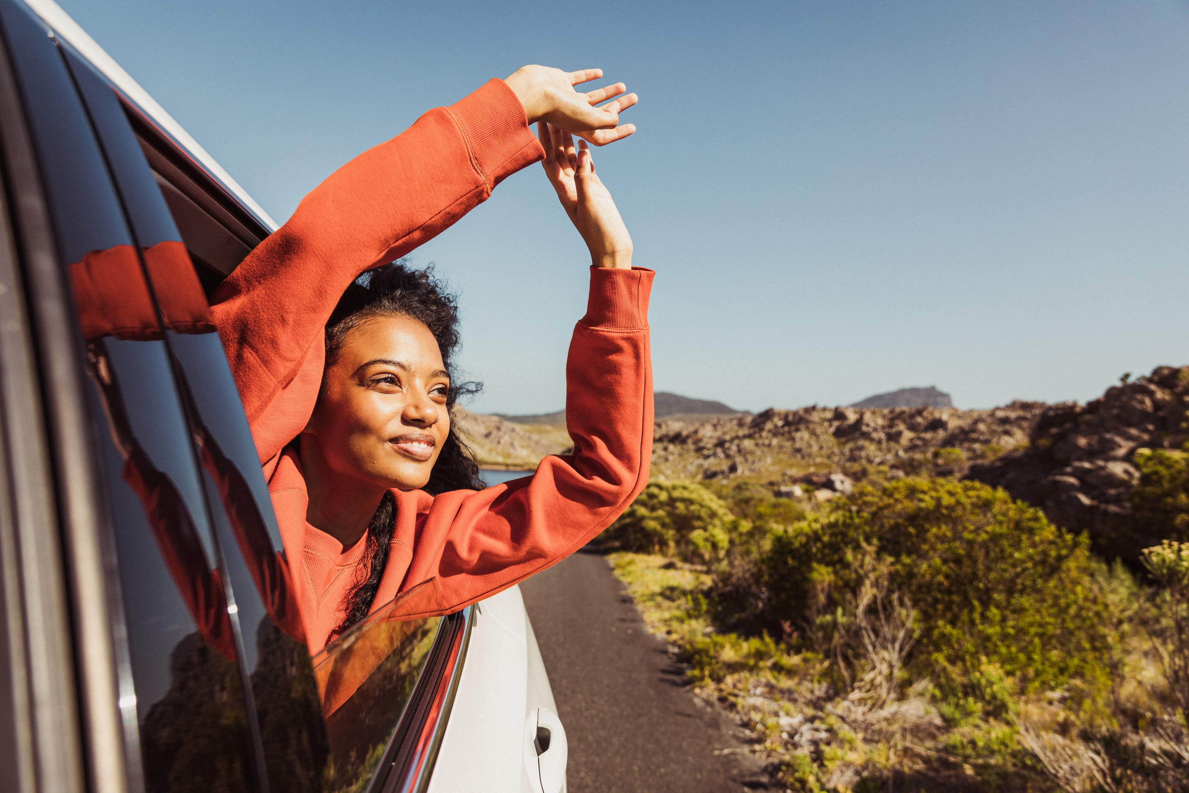 Une femme tend le bras par la fenêtre ouverte de sa voiture.