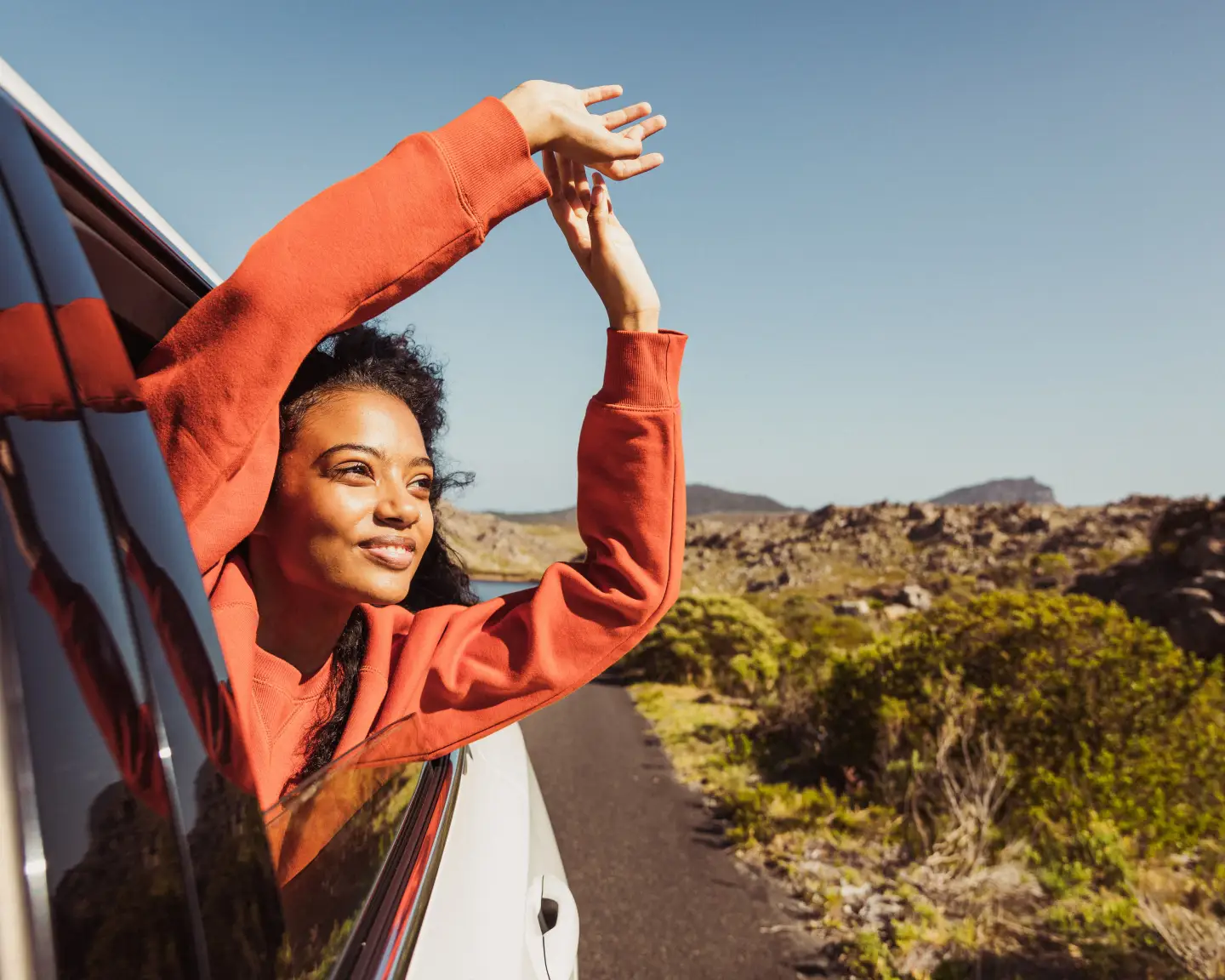 Une femme tend le bras par la fenêtre ouverte de sa voiture.