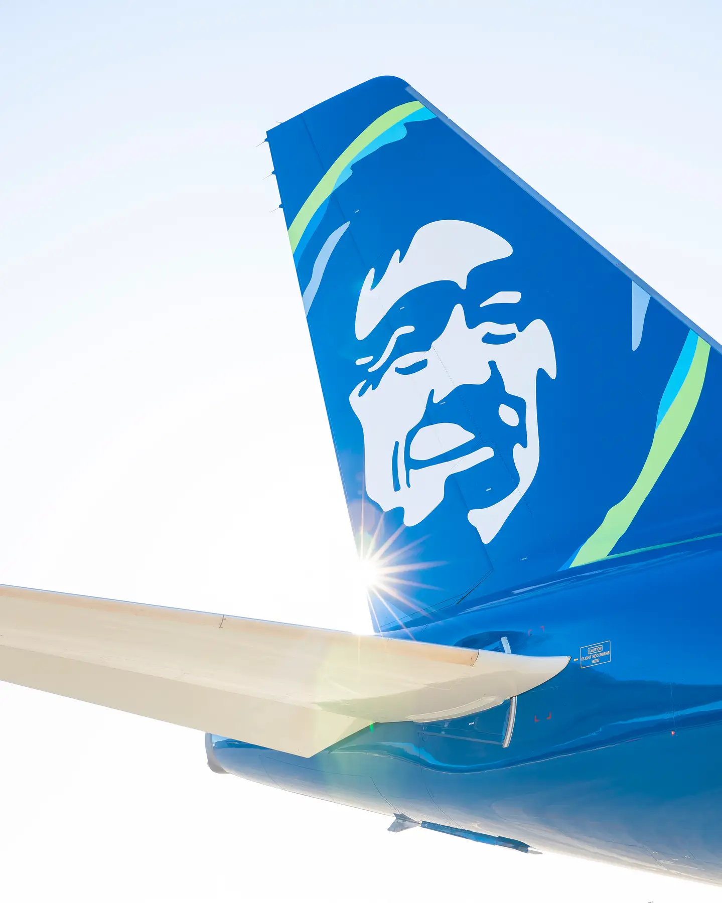 La cola de un avión de Alaska Airlines contra un cielo azul.
