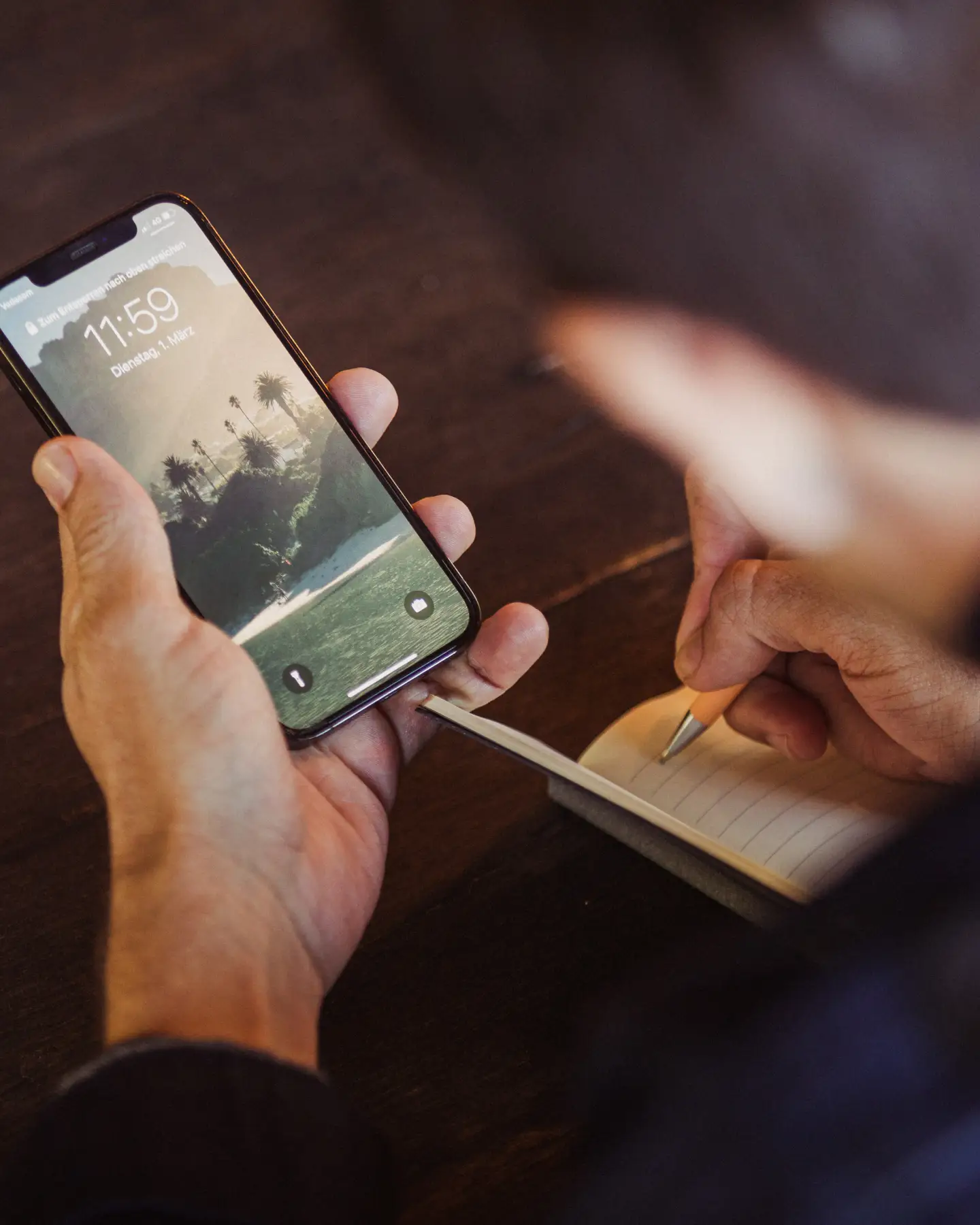 Un hombre sostiene un smartphone y escribe algo en su cuaderno al mismo tiempo.