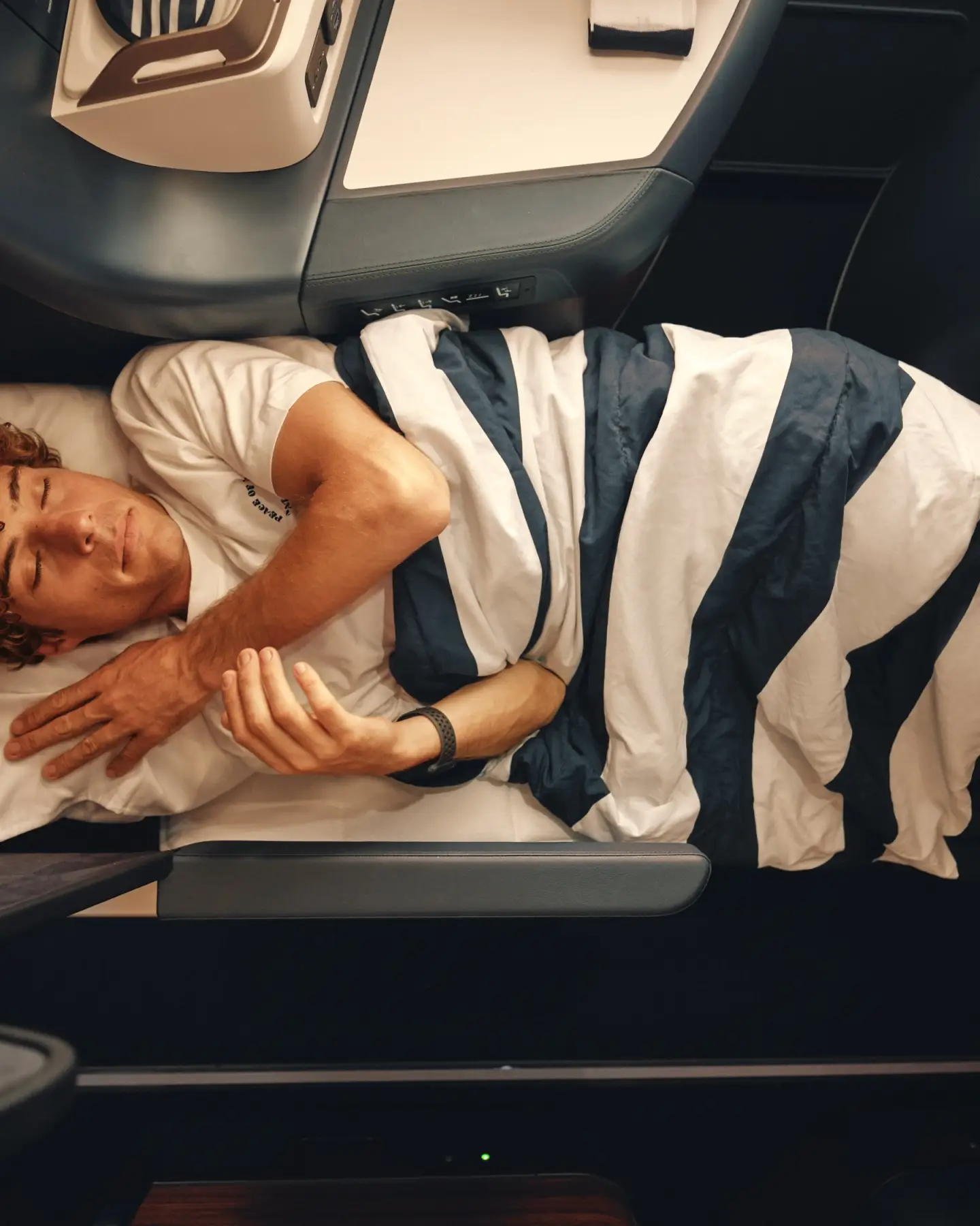 Egy férfi egy csíkos takaró alatt alszik egy Business Class osztályú ülőhelyen