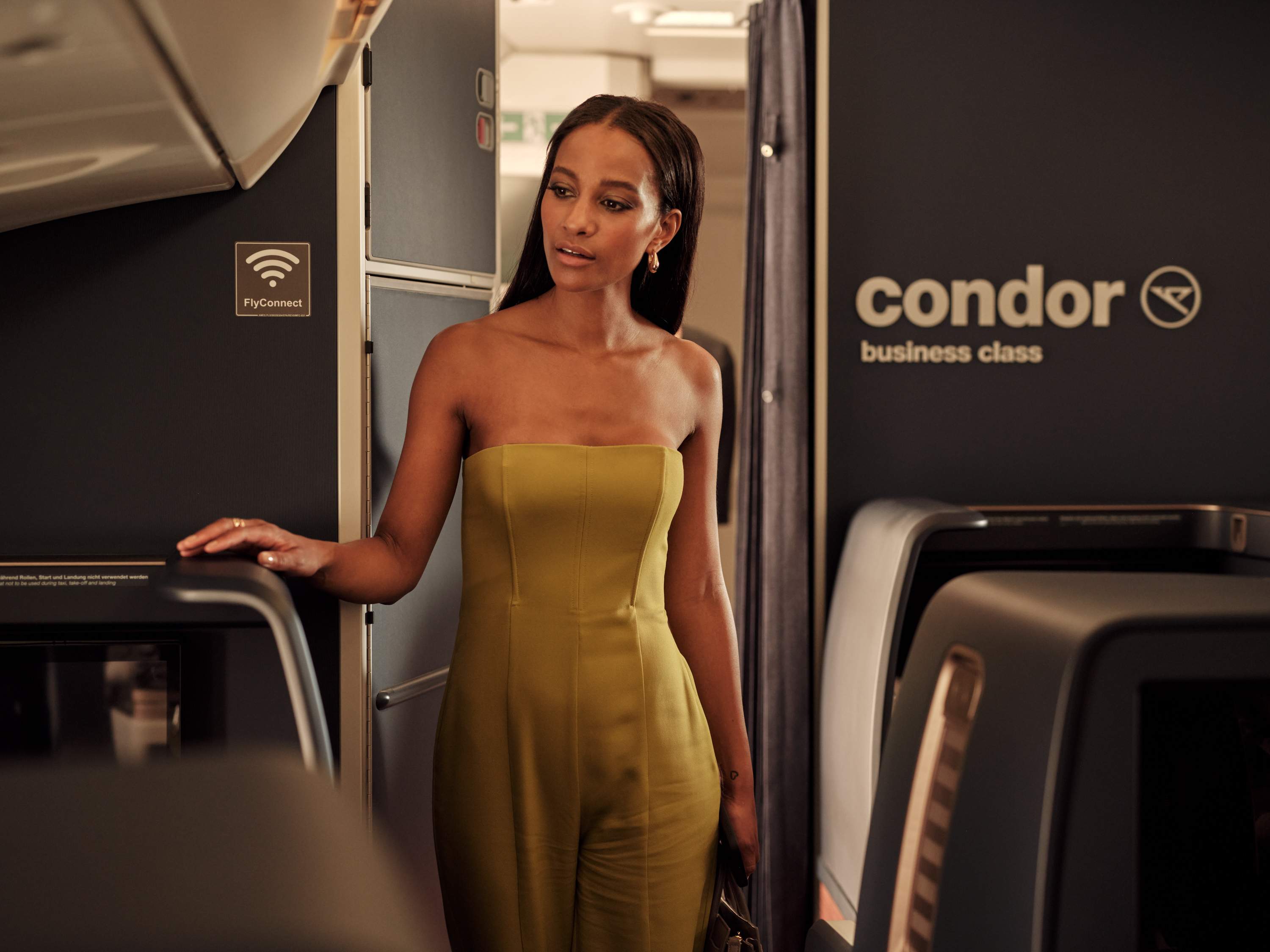 Une jeune femme en robe jaune marche dans la cabine Business Class d’un avion Condor A330 Neo.