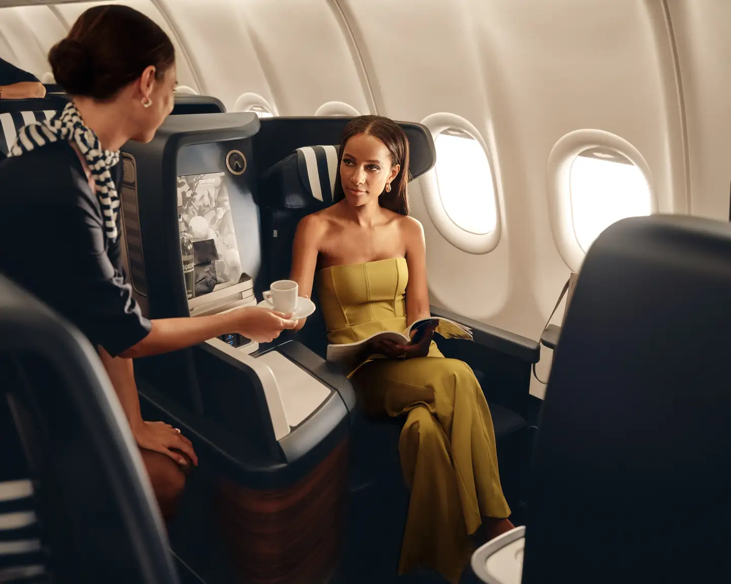 Una mujer sentada en la Business Class a bordo de un avión recibe un café de un auxiliar de vuelo.