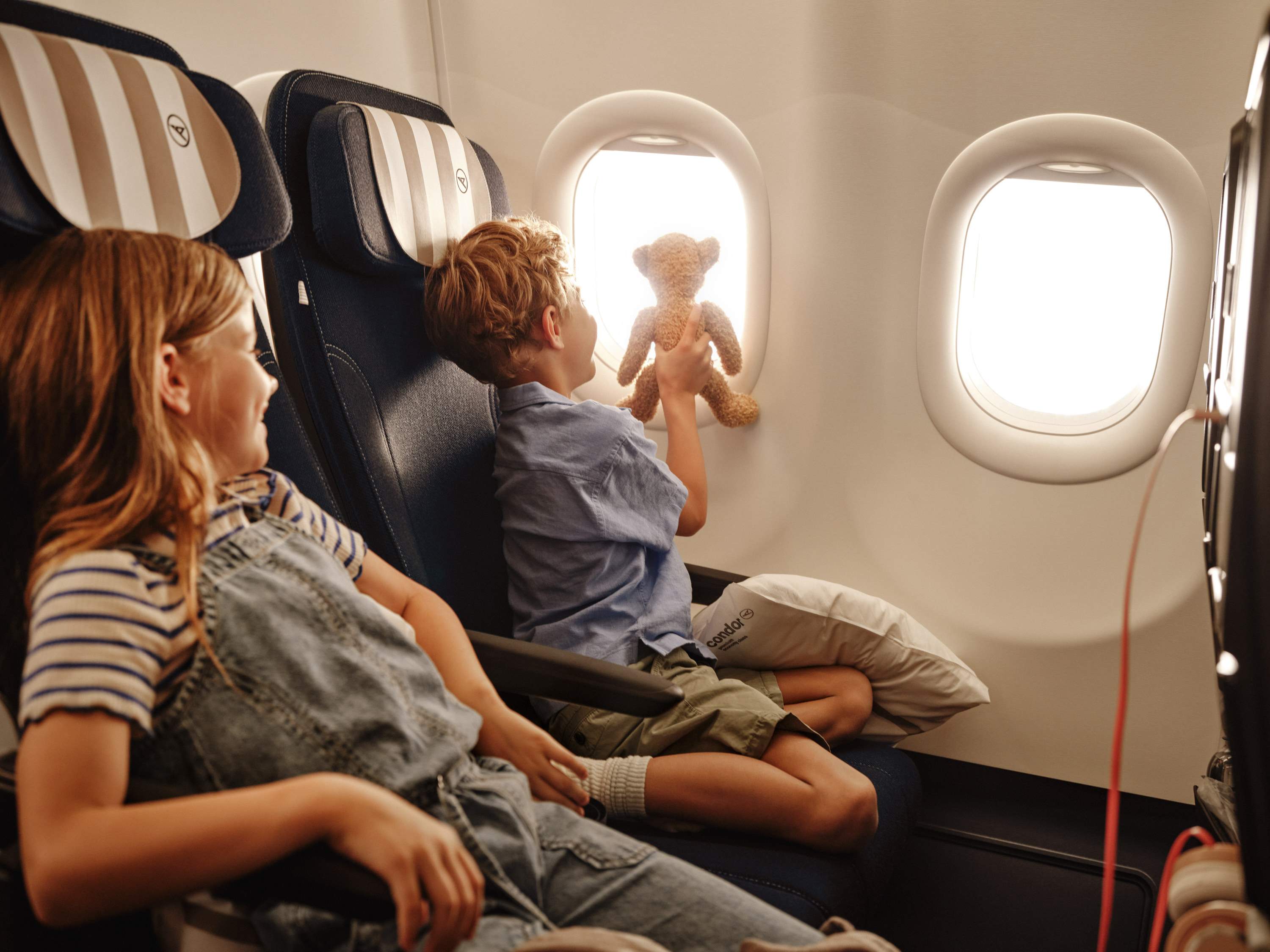 Dos niños están sentados a bordo de un avión de Condor, uno de ellos mira por la ventana.