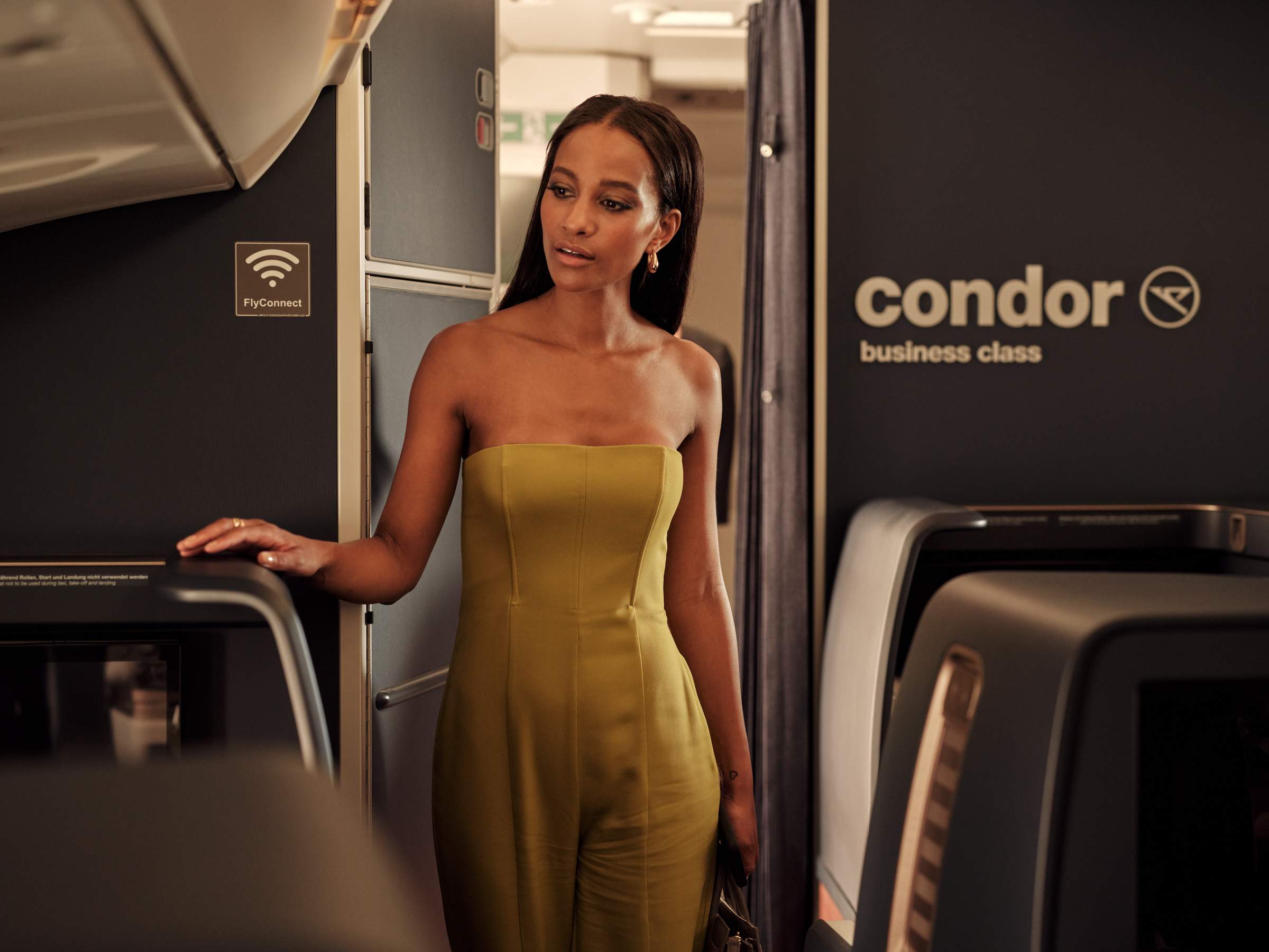 Una joven con un vestido amarillo camina por la cabina de Business-Class de un avión A330 Neo de Condor.