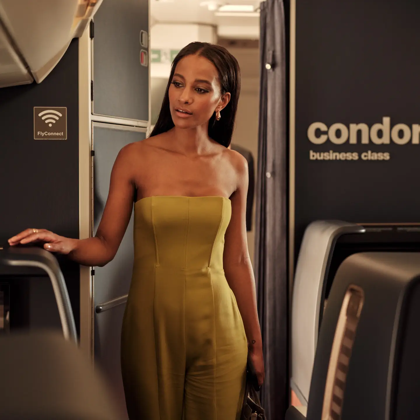 A young woman in a yellow dress is walking through the Business-Class cabin of a Condor A330 Neo plane.