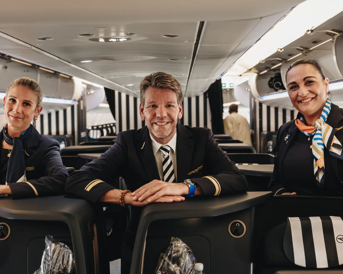 Crew members on board a Condor aircraft look at the viewer with a smile.