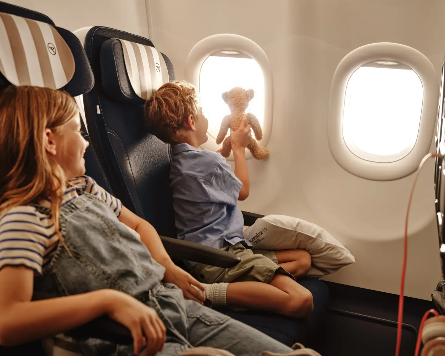 Twee kinderen zitten aan boord van een Condor-vliegtuig, één van hen kijkt uit het raam.