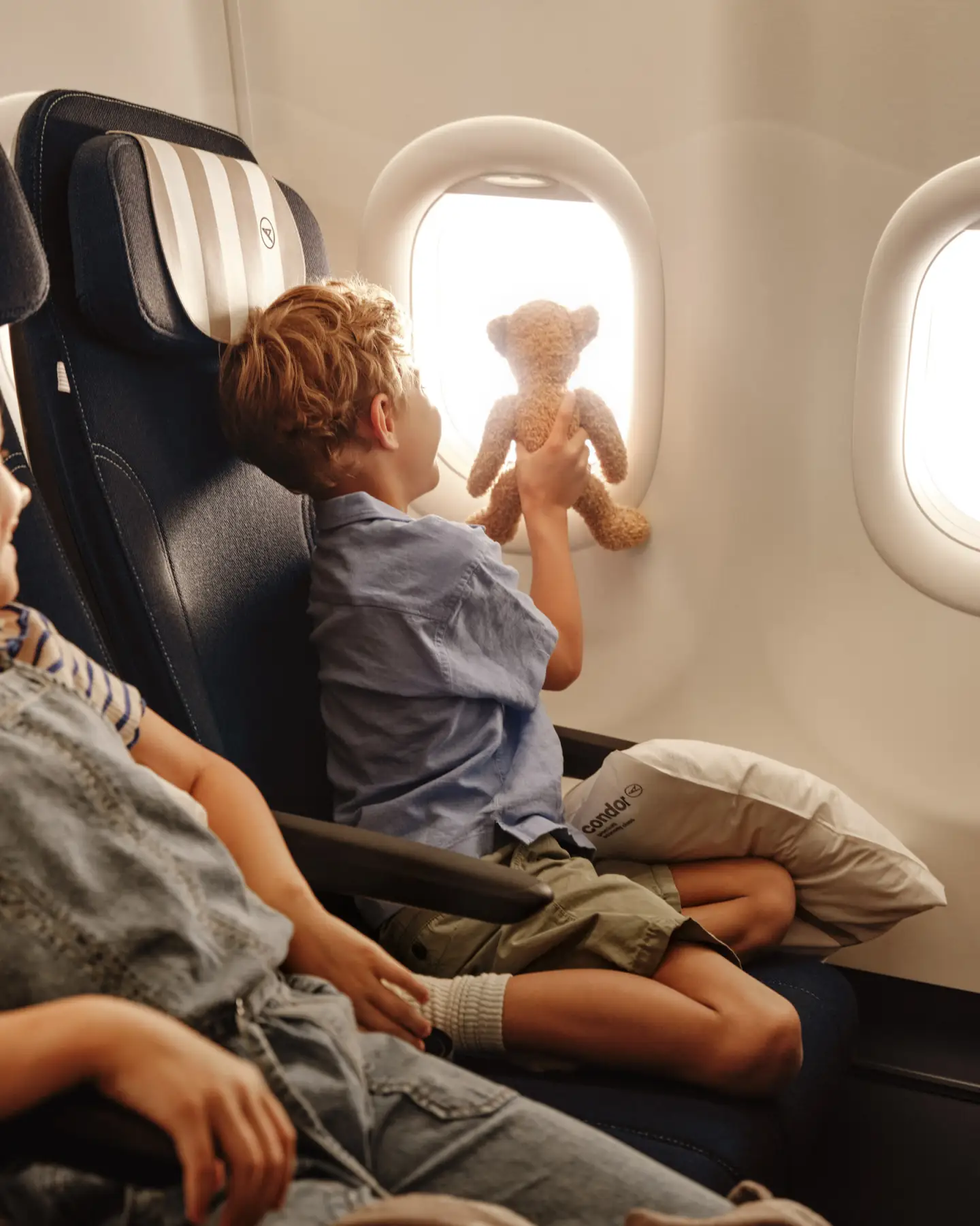 Twee kinderen zitten aan boord van een Condor-vliegtuig, één van hen kijkt uit het raam.