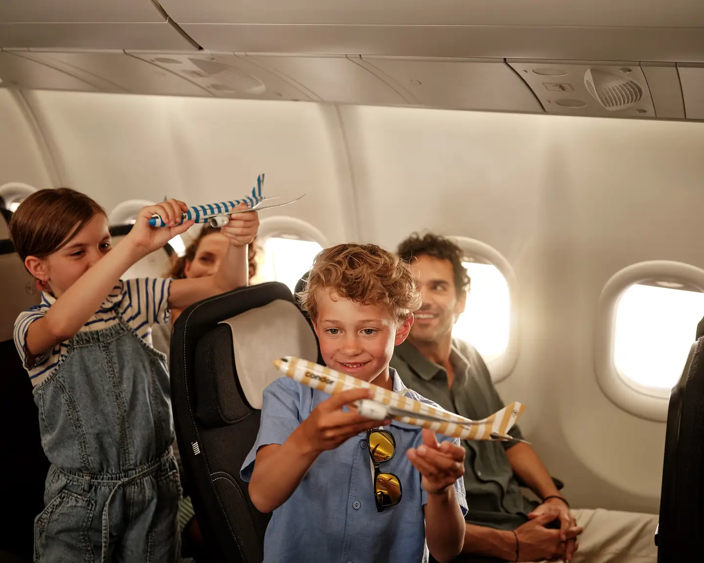 Dos niños juegan con maquetas de aviones Condor con rayas a bordo de un avión Condor, mientras sus padres los observan sonrientes.
