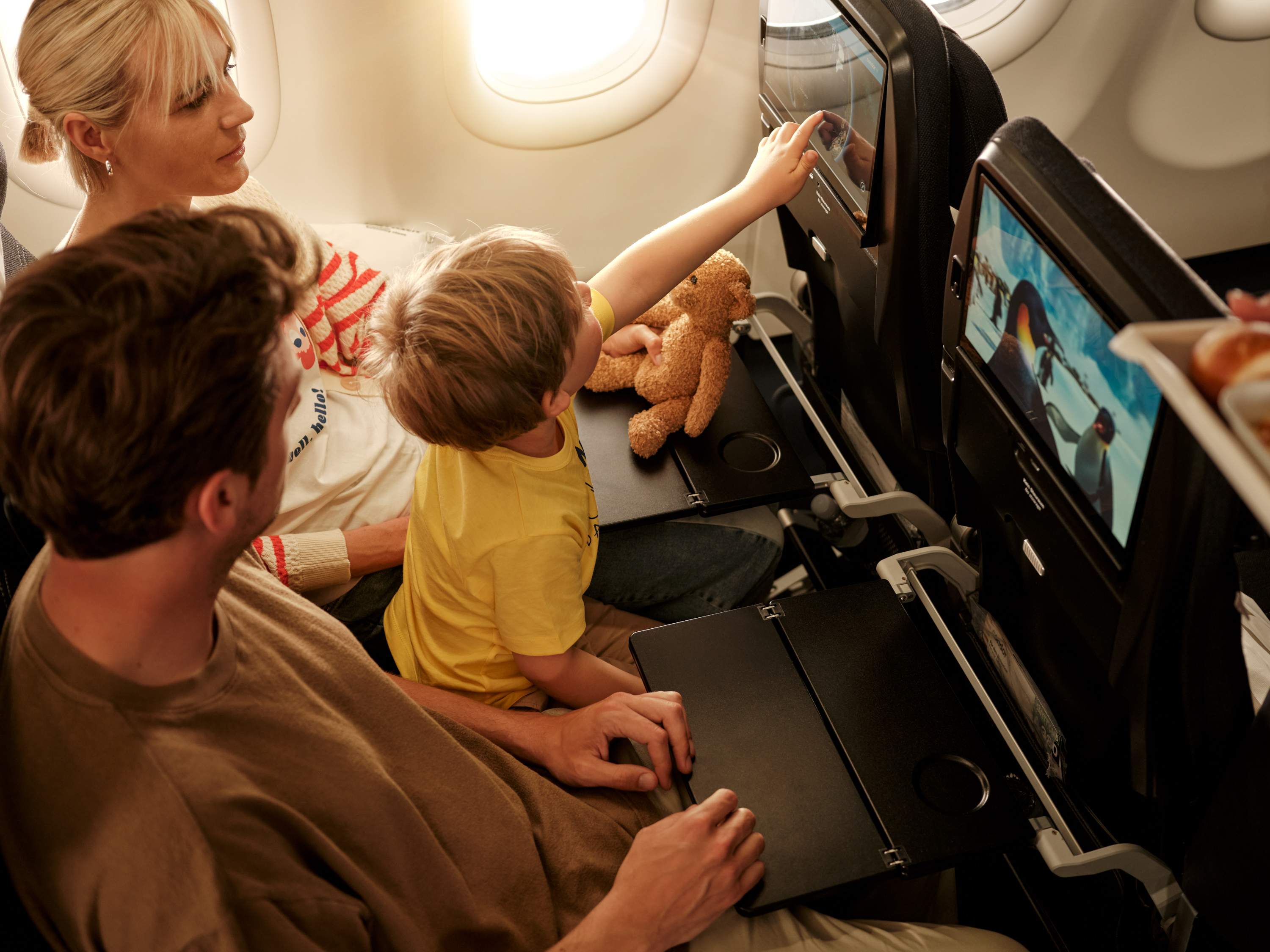 Een kleine jongen op de schoot van zijn ouders wijst naar het inflight entertainmentscherm