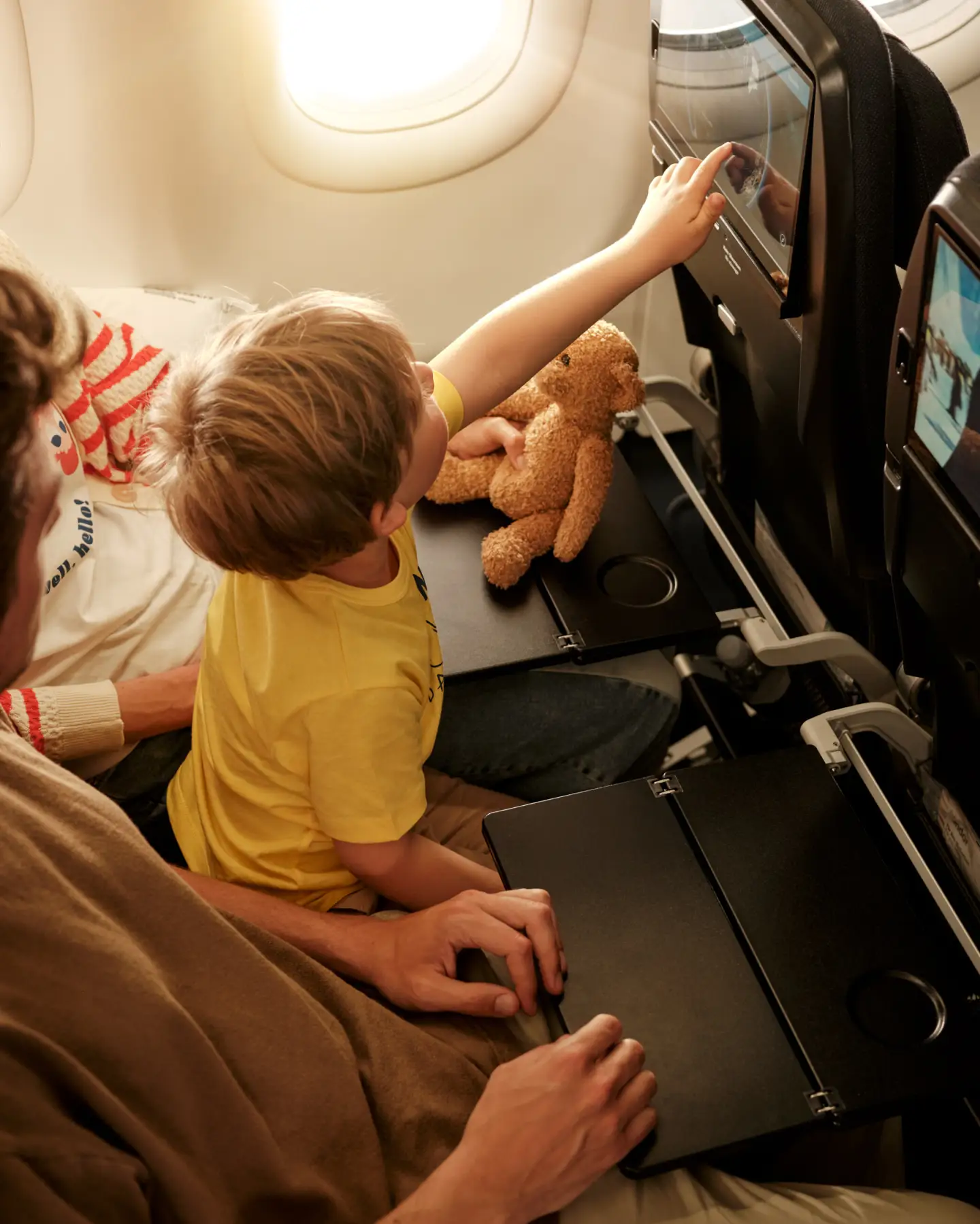 Een kleine jongen op de schoot van zijn ouders wijst naar het inflight entertainmentscherm