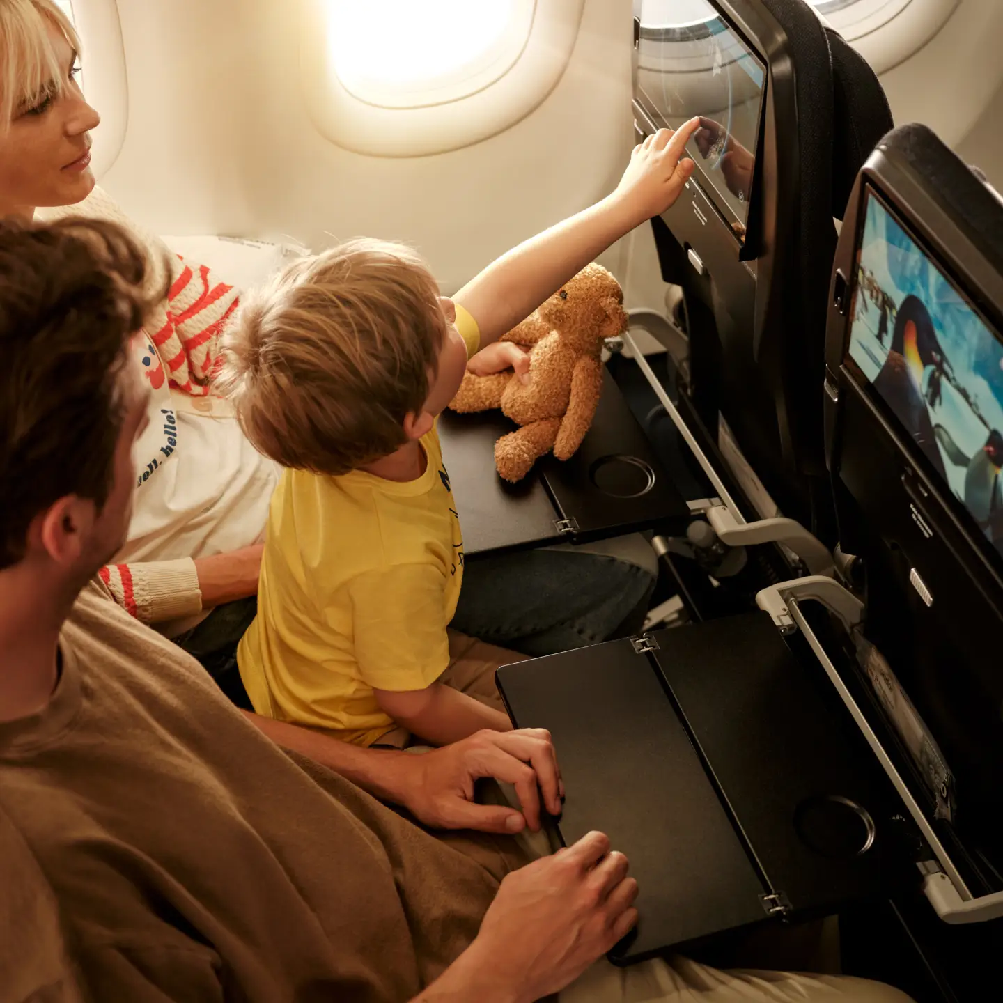 Een kleine jongen op de schoot van zijn ouders wijst naar het inflight entertainmentscherm