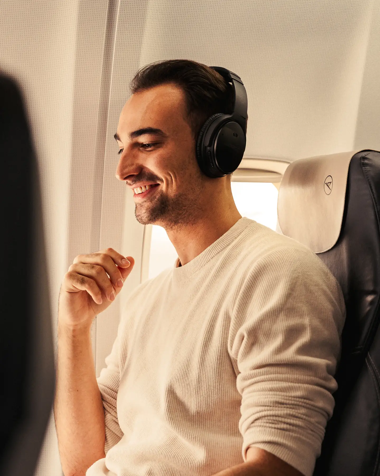 Un hombre con auriculares está sentado relajado y sonriente en un avión.
