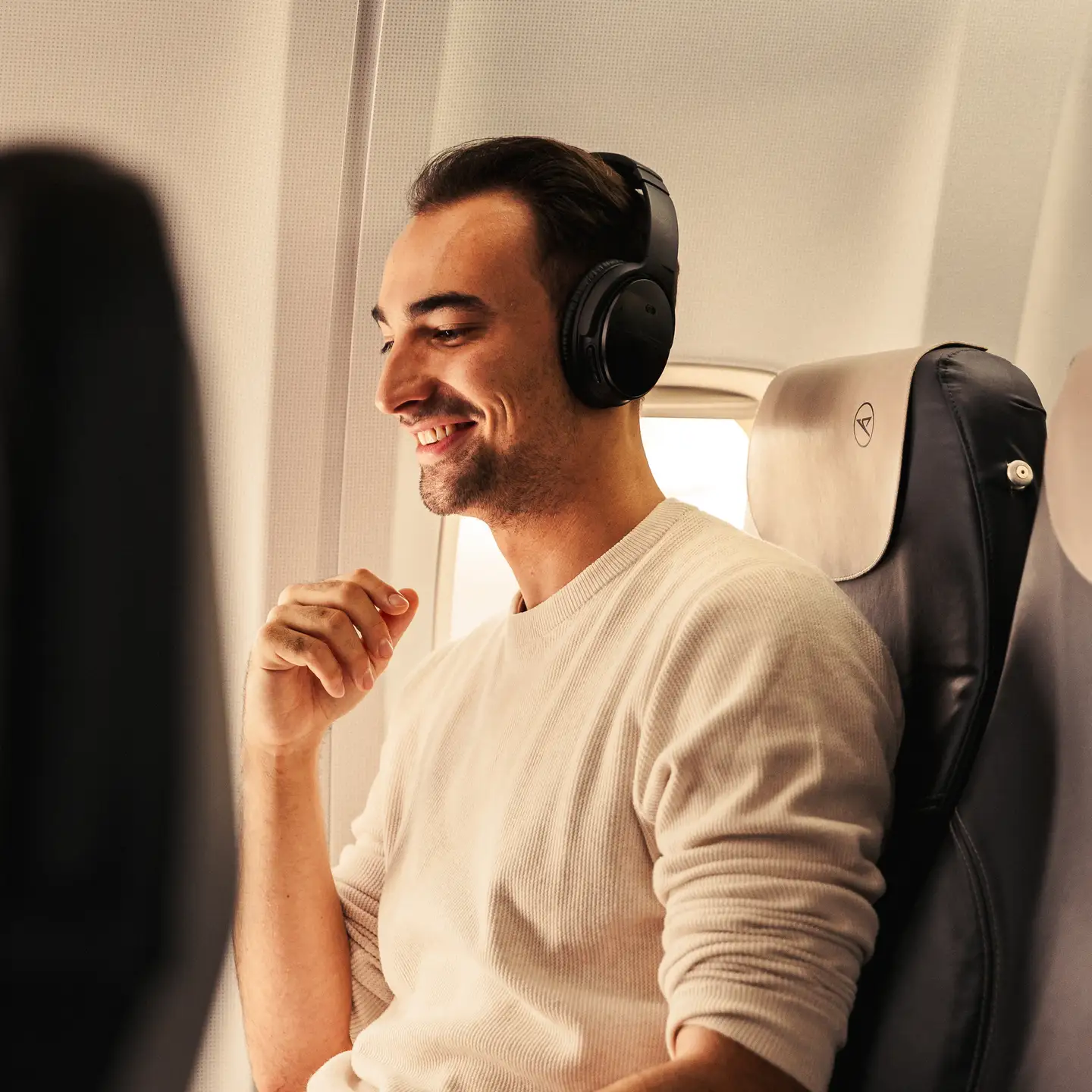 Un hombre con auriculares está sentado relajado y sonriente en un avión.