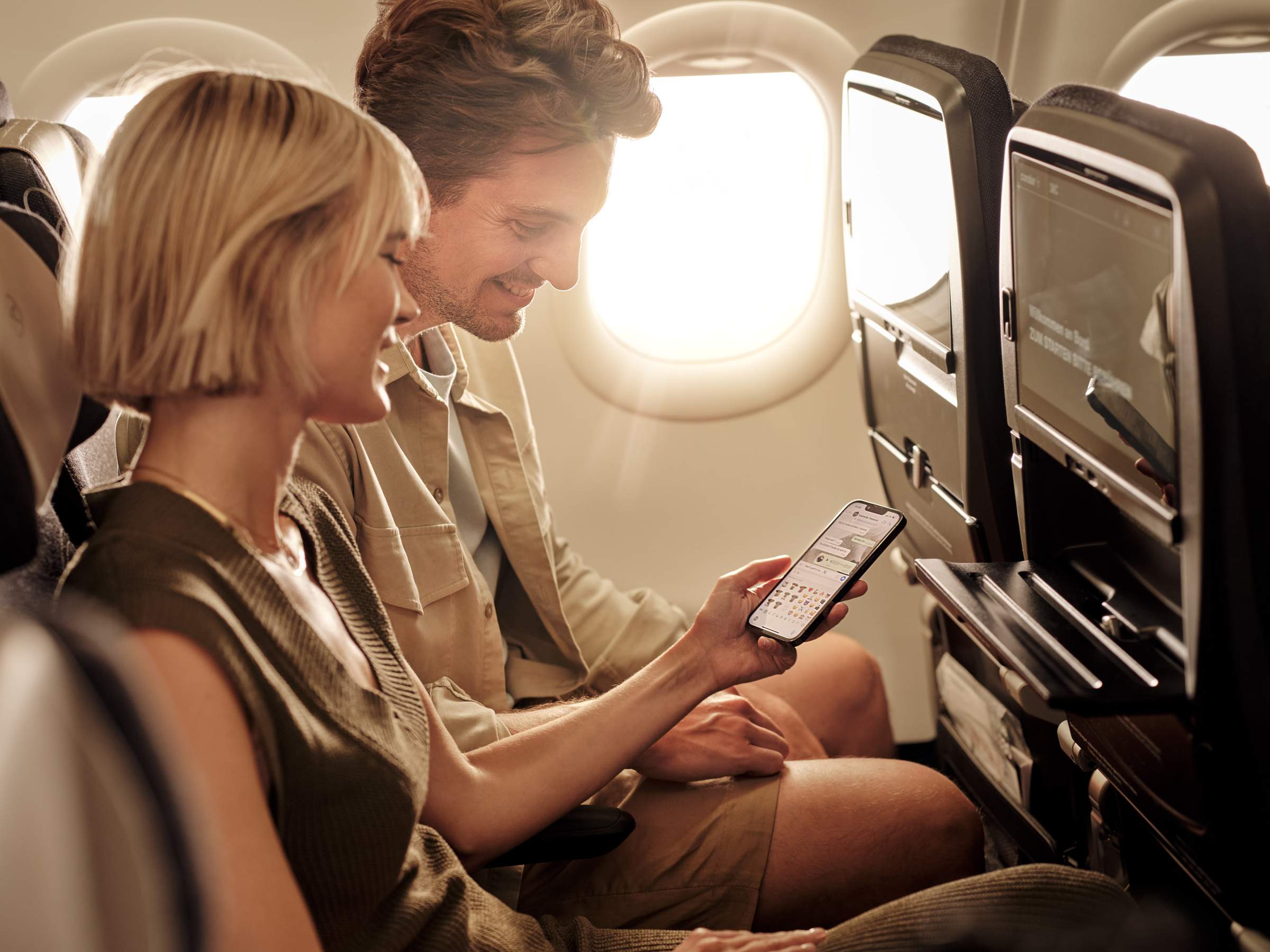 Una pareja está sentada en un avión viendo un chat en su smartphone
