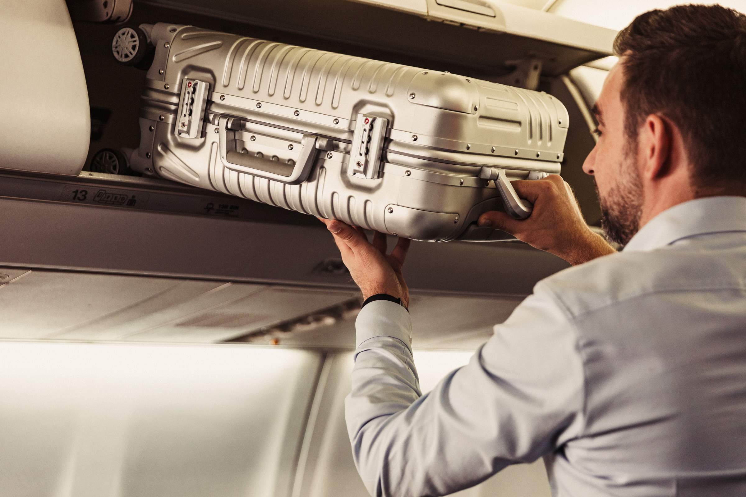 Un hombre está sacando su maleta de mano del compartimento superior que hay sobre su asiento.