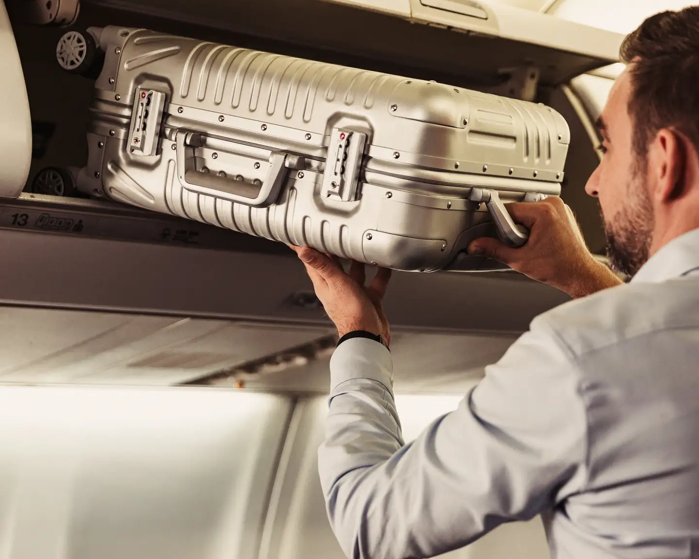 Un hombre está sacando su maleta de mano del compartimento superior que hay sobre su asiento.