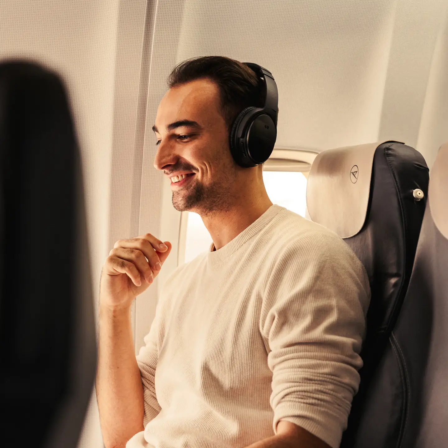 Un hombre con auriculares está sentado relajado y sonriente en un avión.