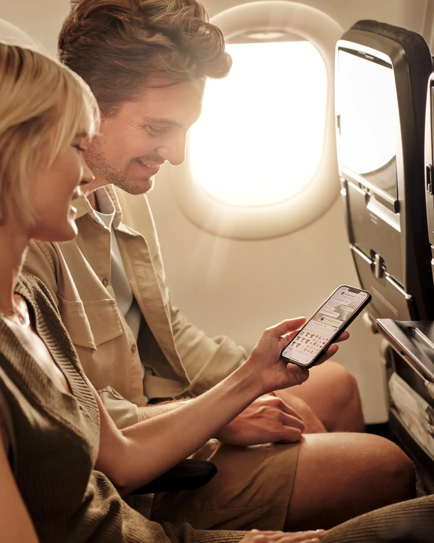 Un couple est assis dans un avion et regarde une discussion sur leur smartphone