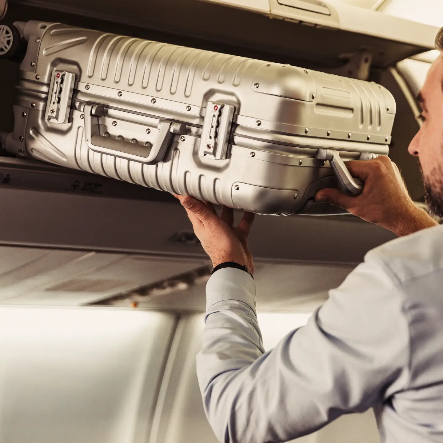 Un homme récupère sa valise à main dans le compartiment au-dessus de son siège