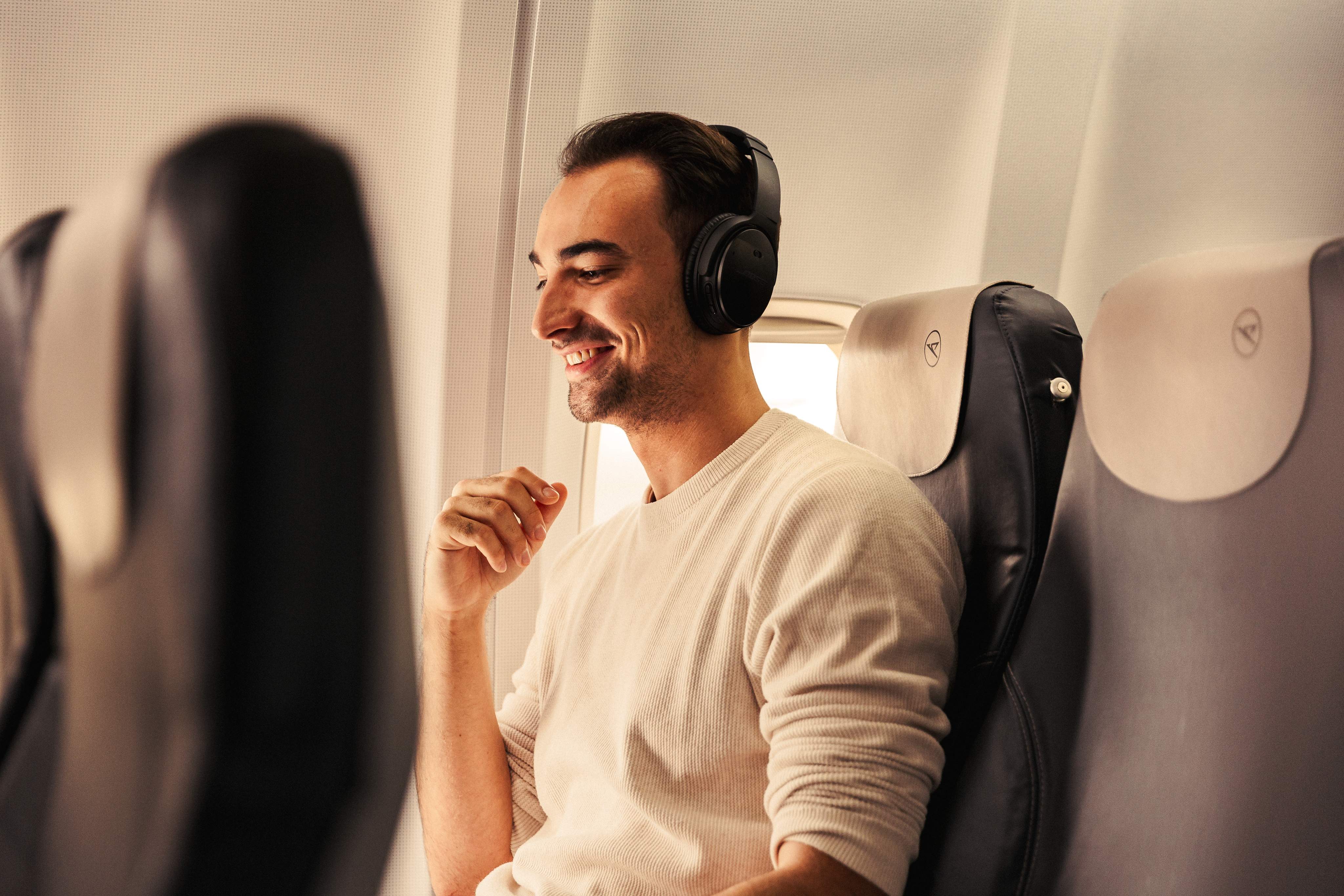 Un homme portant des écouteurs est assis, détendu et souriant, dans un avion.