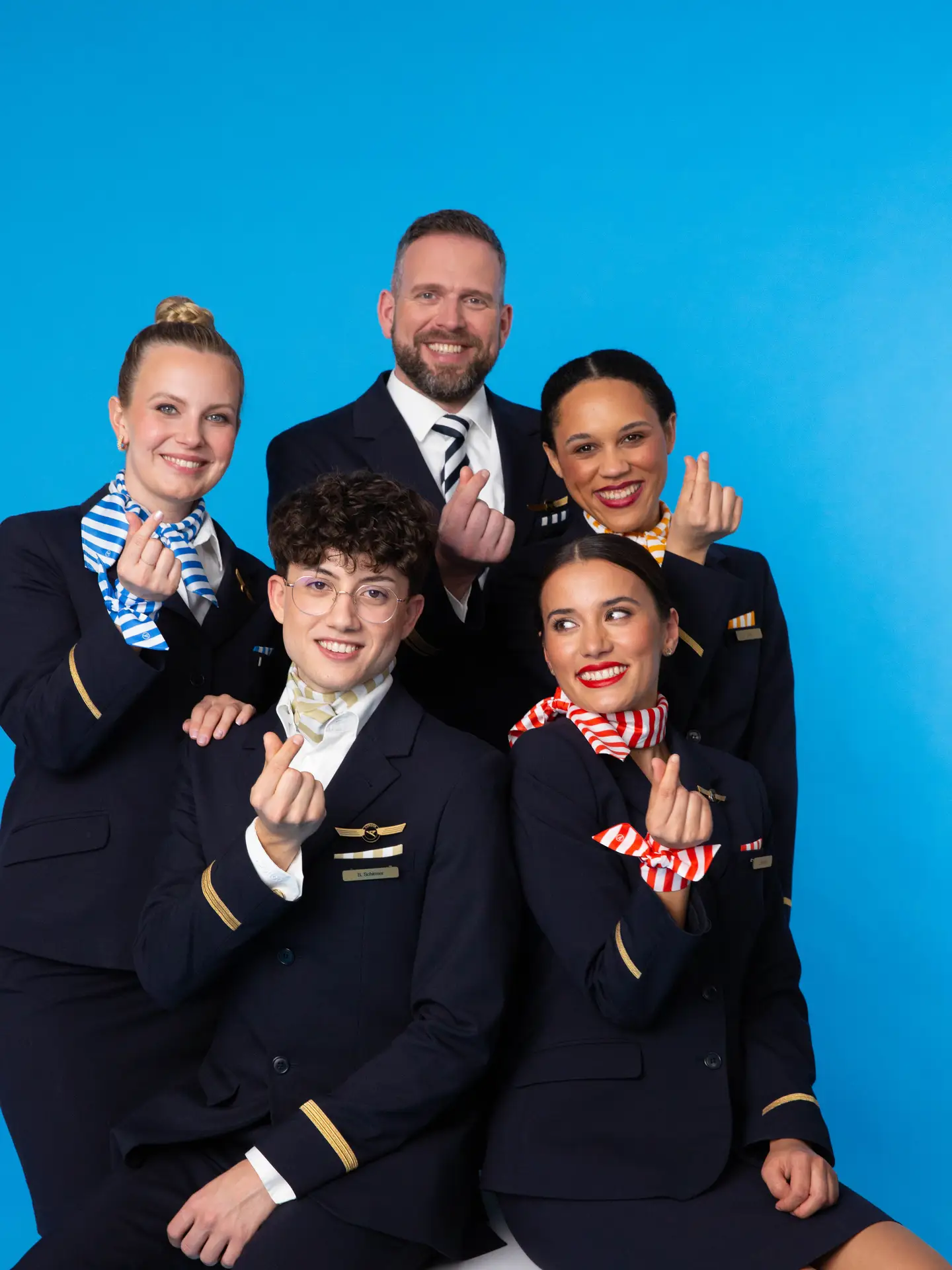 La tripulación de Condor con auxiliares de vuelo, sobrecargo y piloto frente a un fondo azul marino con uniformes y accesorios a rayas