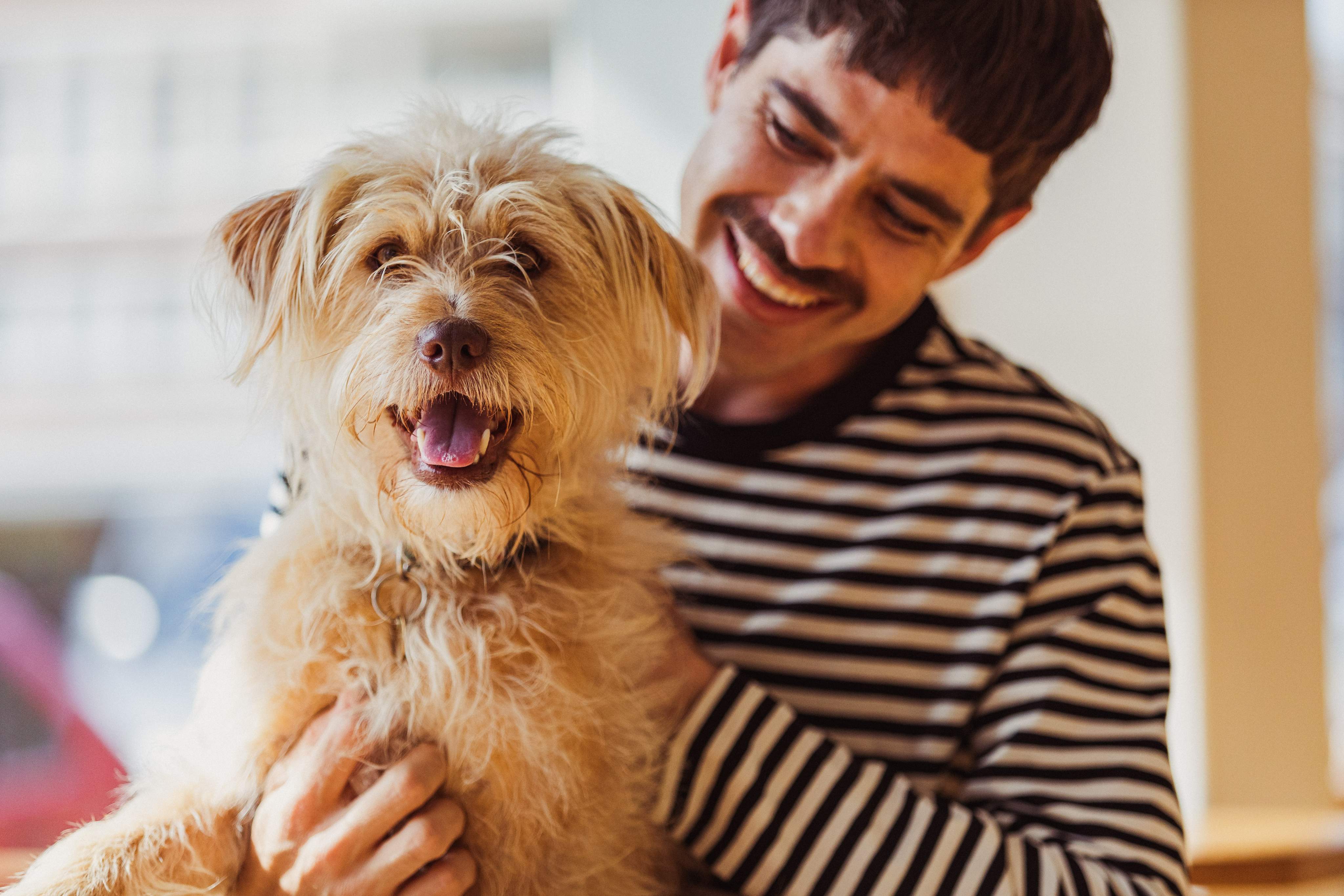 Hombre sosteniendo un perro en su regazo y sonriendo a la cámara