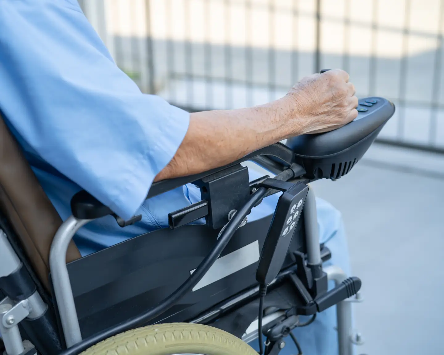 Close-up of an elderly person operating an electric wheelchair using a control panel.