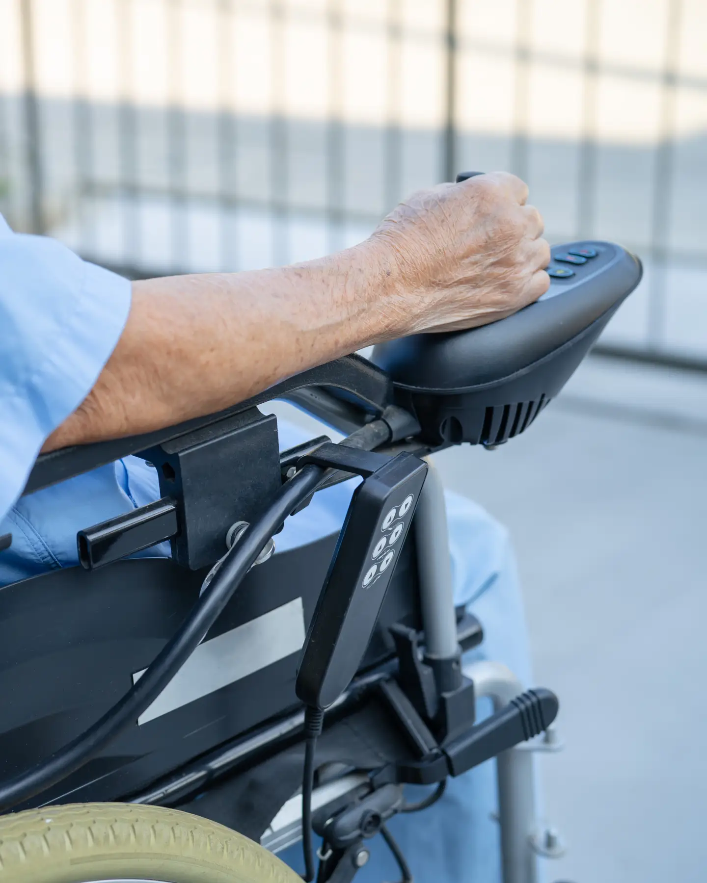 Close-up van een oudere persoon die een elektrische rolstoel bedient met behulp van een bedieningspaneel.