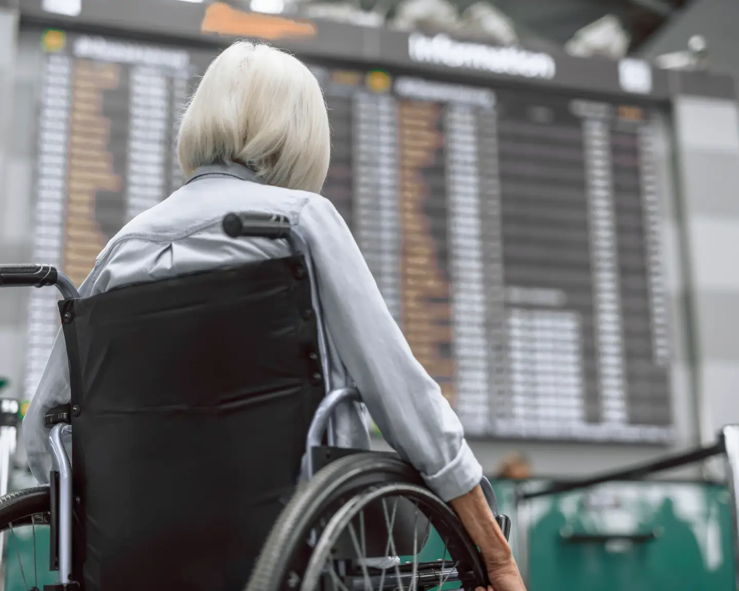 Un voyageur en fauteuil roulant consulte les horaires d'arrivée et de départ sur un écran dans le hall des départs d'un aéroport.