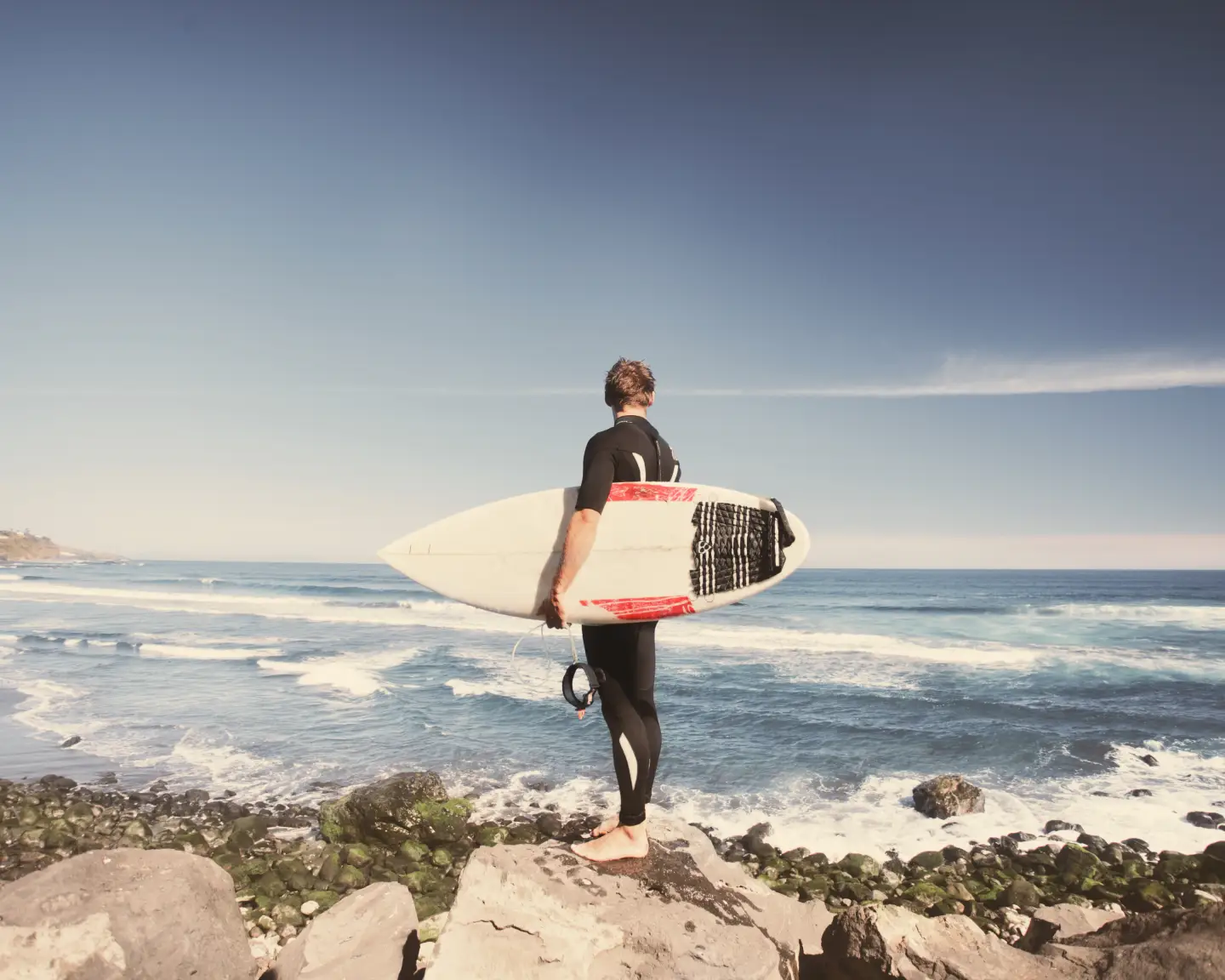 A man is standing with his surfboard by the sea