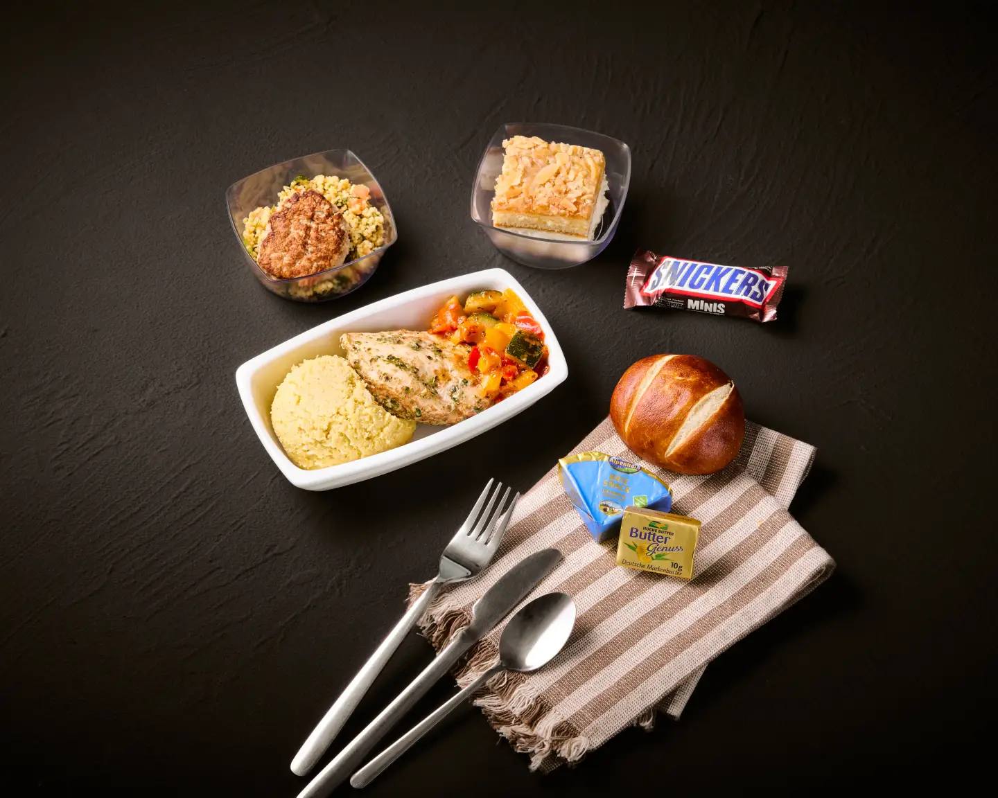 Een maaltijd aan boord bestaande uit gegrilde kip met groenten, couscous, een bijgerecht salade, een schaaltje dessert, kaas en een Snickersreep.