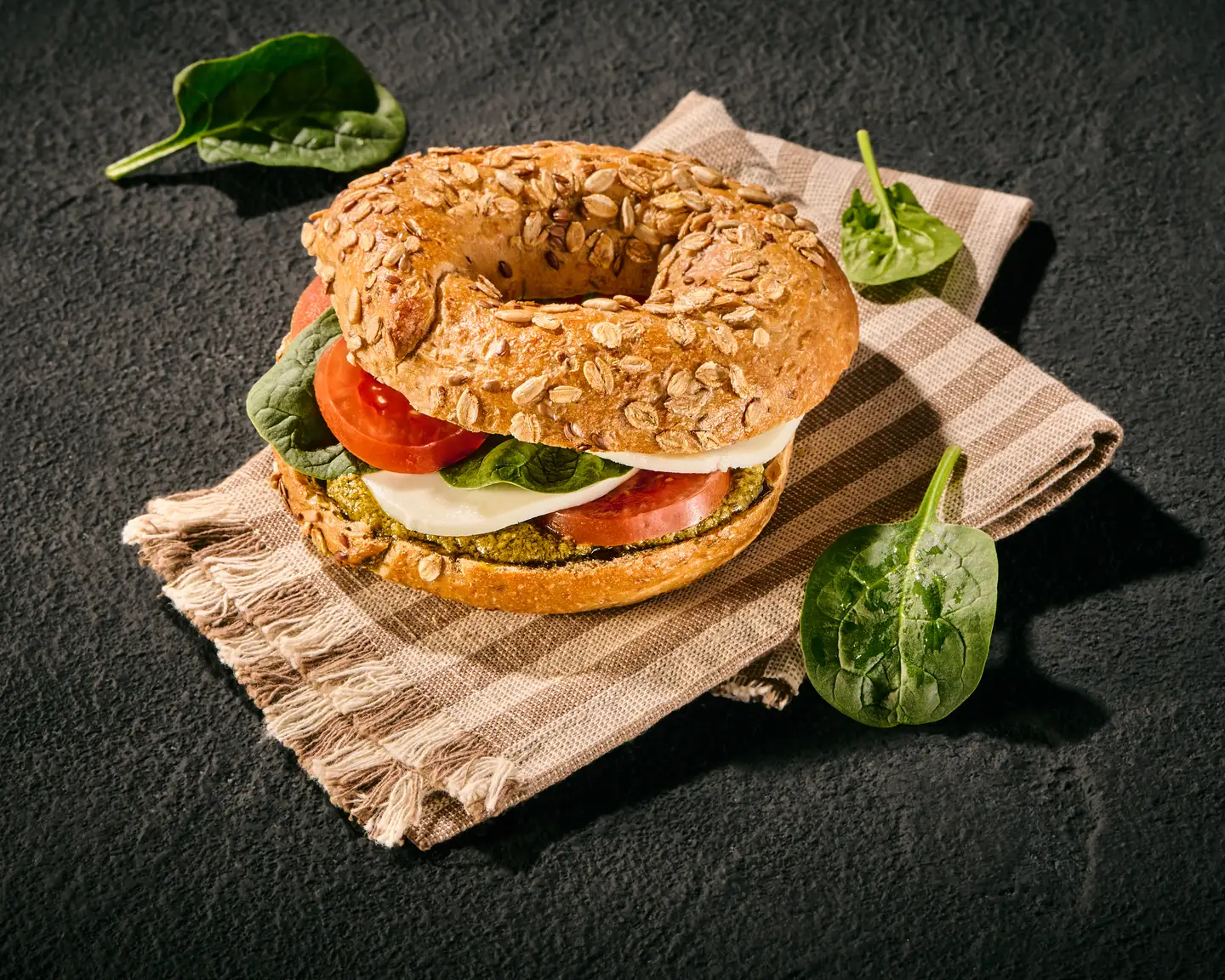 Bagel de semillas cubierto con tomate y mozzarella, servido sobre una servilleta a rayas