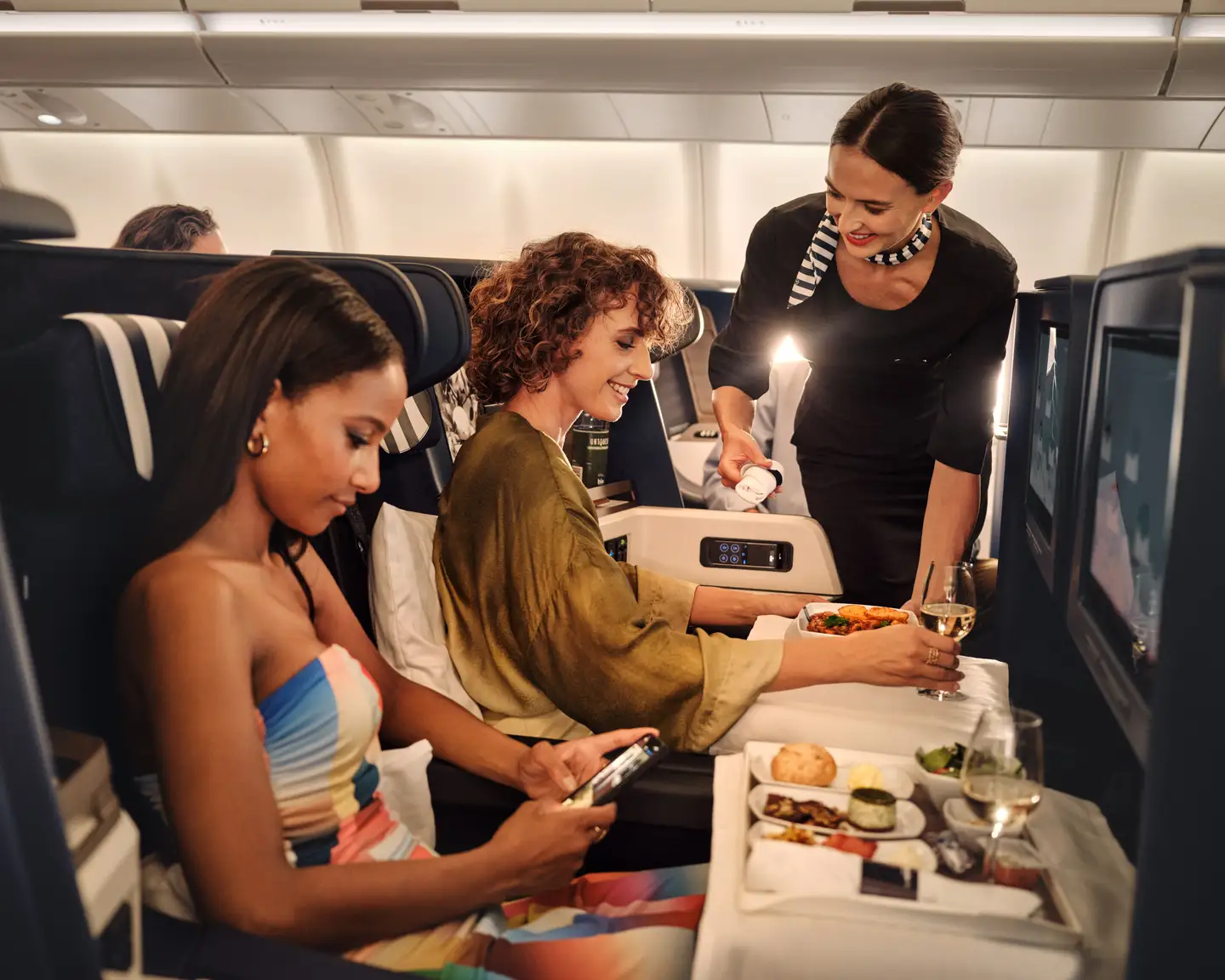 Una auxiliar de vuelo sirve comida a dos pasajeras en Business Class.
