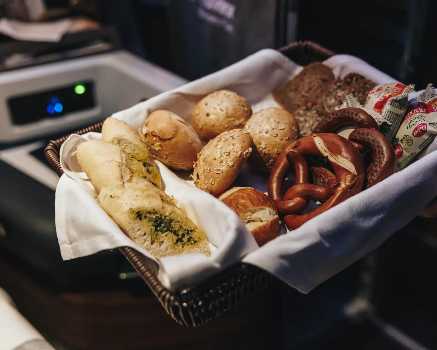 Una cesta de pan con pretzels y panecillos sostenida por una auxiliar de vuelo.