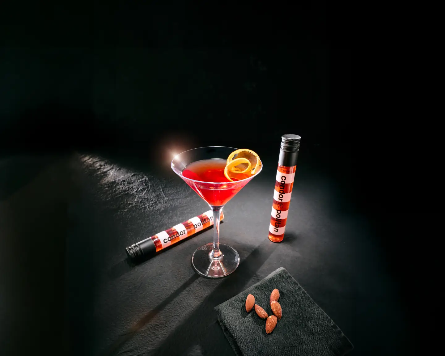 Sklenice na martini obsahující červený koktejl vedle podlouhlé červenobíle pruhované láhve.