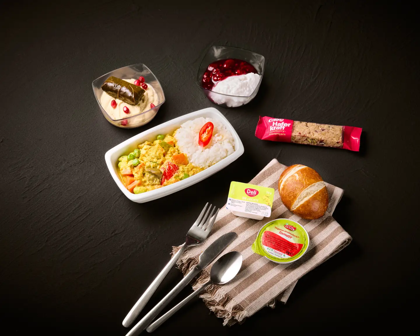 Una comida servida en un avión que incluye una porción de paella, una ensalada con pepino encurtido, un yogur, un panecillo, una manzana y una barrita de muesli.