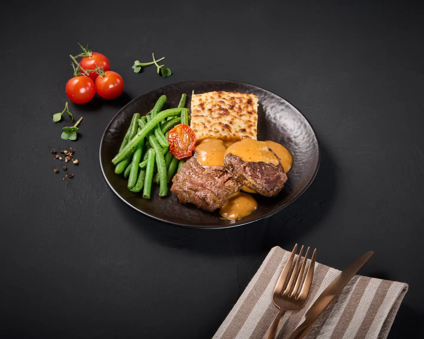 Carne braseada con salsa de crema de pimienta, gratinado de papas y judías presentadas en un plato